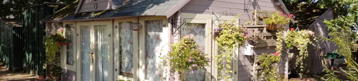 A wooden building with hanging baskets and flowers used relaxing in at our horticulture and conservation project